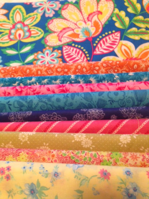 Stack of folded colorful floral and patterned fabrics in blue, pink, orange and yellow tones, vibrant and crafty mood