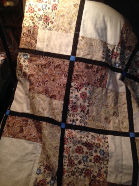 Patchwork quilt with brown, cream, and floral fabric squares divided by black sashing and small blue accent squares, warm handmade feel