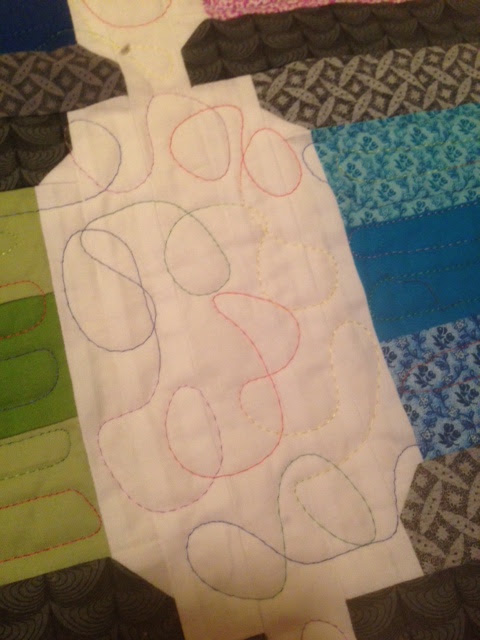 Close-up of quilted fabric with colorful swirling stitch patterns in pink, blue, yellow, and green thread on white and pale fabrics