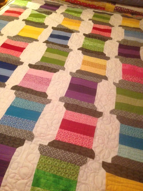 Patchwork quilt with a spool-of-thread pattern in multicolored stripes of pink, green, purple, blue, yellow and gray on white